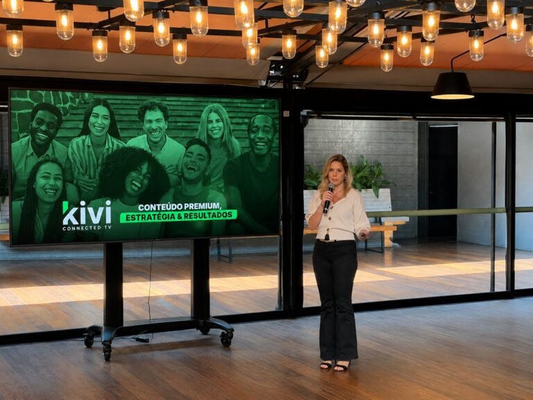 Thays Panar, diretora comercial da Kivi, apresenta conteúdo da empresa ao lado de uma tela com a marca Kivi Connected TV