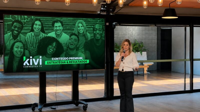 Thays Panar, diretora comercial da Kivi, apresenta conteúdo da empresa ao lado de uma tela com a marca Kivi Connected TV
