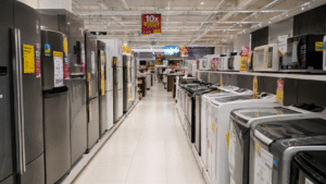 Corredor de loja de eletrodomésticos com geladeiras, lavadoras e micro-ondas expostos, além de diversas etiquetas de promoção e parcelamento