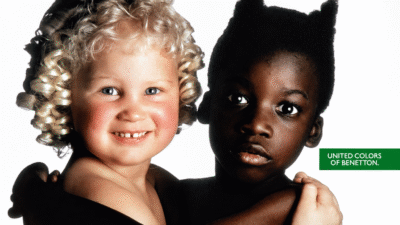 Duas crianças aparecem abraçadas em um anúncio da Benetton de 1991: uma menina branca, loira e de cachos claros, e uma criança negra com o cabelo estilizado em pontas, em composição que ficou conhecida como Angel & Devil.