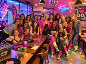 Grupo de mulheres em releitura inspirada nos anos 80, com roupas neon, ombreiras, polainas e cabelos volumosos