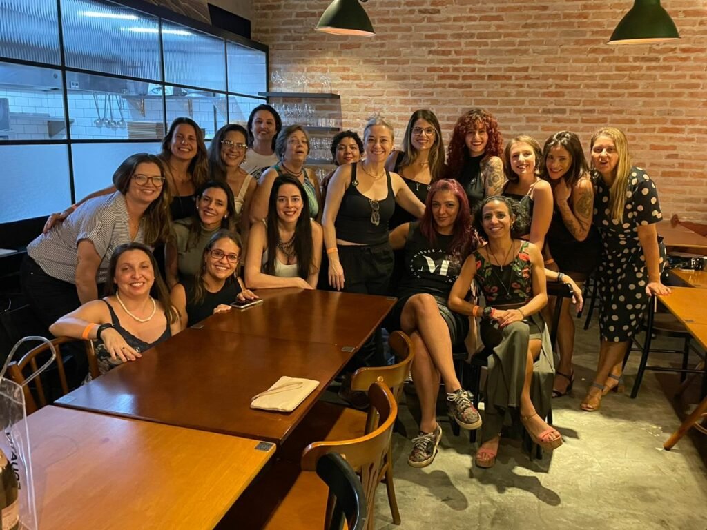 Imagem inspirada na trend dos anos 80, que recria fotos com estética dos anos 80. Um grupo de mulheres aparece com roupas e acessórios neon, ombreiras marcadas, polainas e penteados volumosos típicos da década