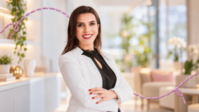 Gabriela Dias sorri para a câmera, de braços cruzados, em retrato horizontal com detalhe de linha bordada lilás