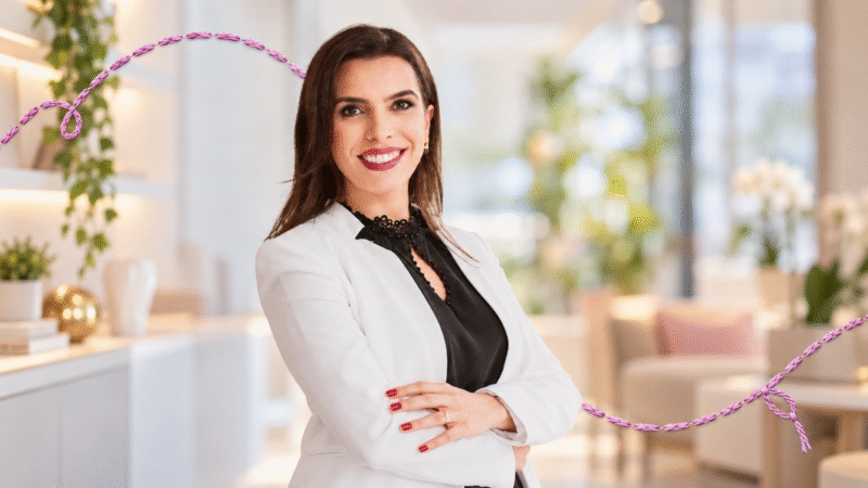Gabriela Dias sorri para a câmera, de braços cruzados, em retrato horizontal com detalhe de linha bordada lilás